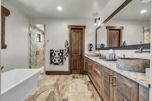 Full bath with double vanity, a stall shower, a freestanding bath, recessed lighting, and light marble finish flooring