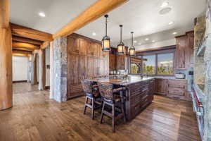 Kitchen with a kitchen island, dark stone counters, dark wood-style floors, pendant lighting, and beam ceiling