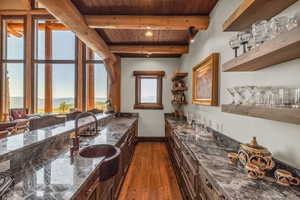 Kitchen with dark wood-style flooring, open shelves, dark stone counters, and a wood ceiling with exposed beams