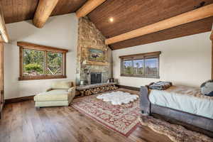 Bedroom featuring wood-type flooring, a stone fireplace, recessed lighting, and a high wood beamed ceiling