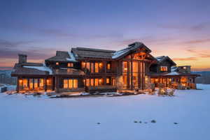 Snow covered house featuring a standing seam roof, a patio area, stone siding, and a chimney