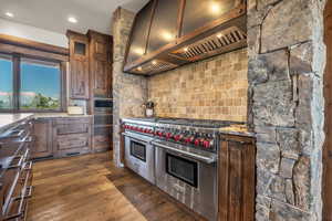 Kitchen with range with two ovens, dark wood finished floors, light stone counters, decorative backsplash, and recessed lighting