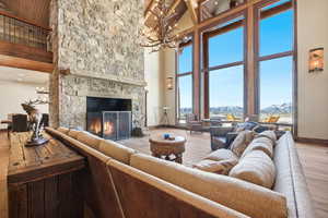 Living room with wood finished floors, a chandelier, a high wooden beamed ceiling, and a stone fireplace