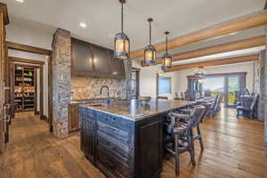 Dual tone kitchen featuring a kitchen bar, tasteful backsplash, an island with sink, dark wood-style flooring, and dark stone countertops