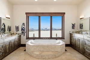 Full bath featuring two vanities, stone tile floors, a bath, a mountain view, and recessed lighting