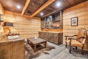 Living area with wooden walls, light wood-style floors, a wooden ceiling with exposed beams, and recessed lighting