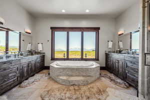 Bathroom featuring two vanities, stone tile flooring, a bath, plenty of natural light, and recessed lighting