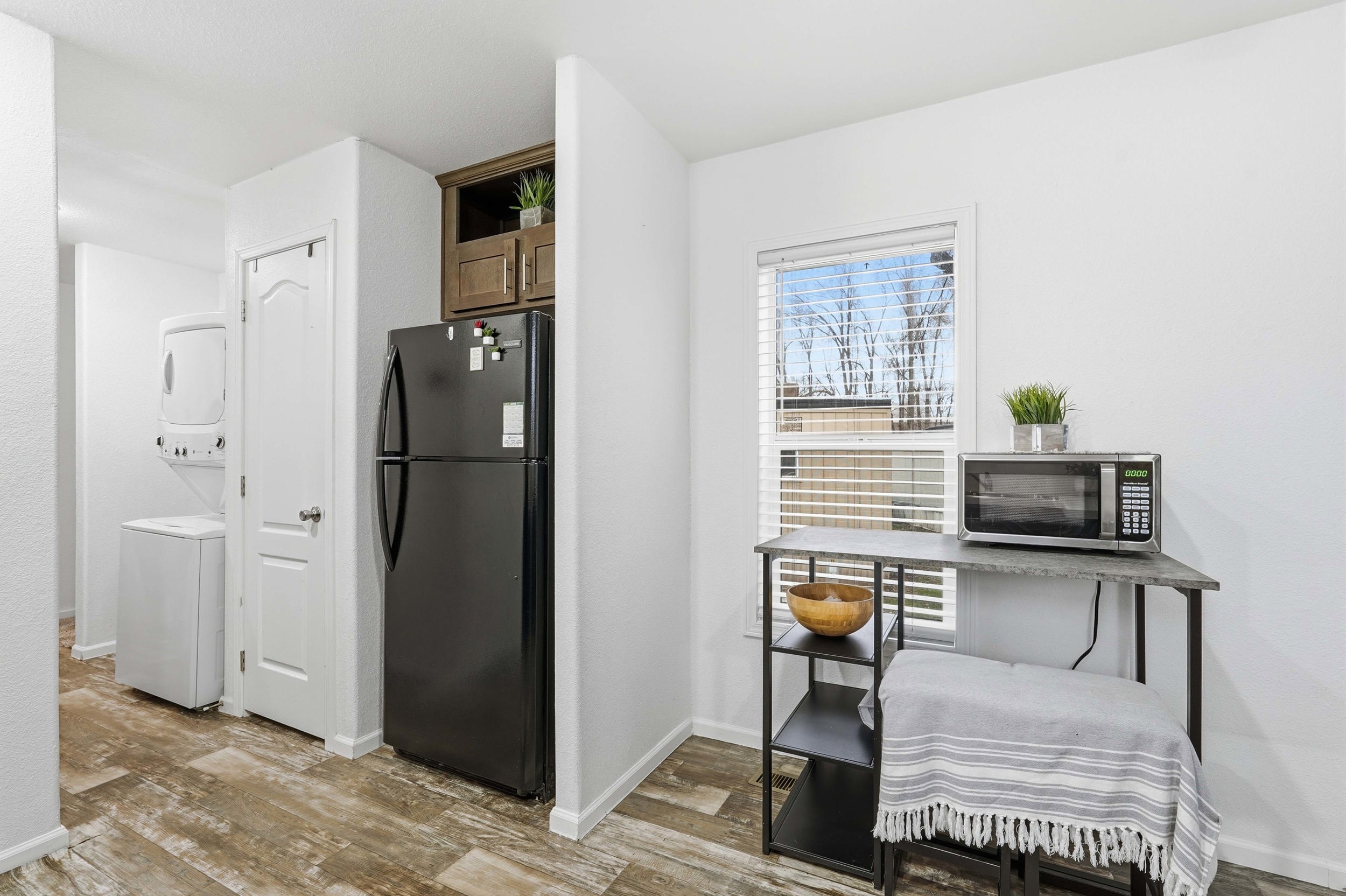 Kitchen with freestanding refrigerator, stainless steel microwave, light wood-type flooring, stacked washer / dryer, and open shelves