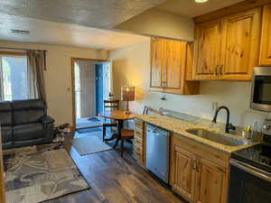 Kitchen featuring stainless steel appliances, light stone countertops, dark wood finished floors, a textured ceiling, and open floor plan