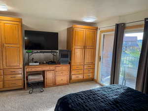 Bedroom with access to outside, light carpet, a desk, and a textured ceiling