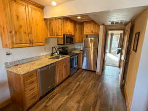 Kitchen featuring stainless steel appliances, light stone countertops, wood finish cabinets, dark wood-type flooring, and a textured ceiling