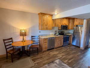 Kitchen featuring stainless steel appliances, light stone counters, a textured ceiling, and dark wood-style floors