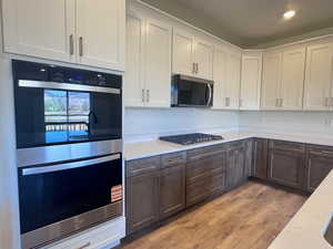 Kitchen with dual tone cabinets, stainless steel appliances, light wood-style flooring, light stone countertops, and recessed lighting