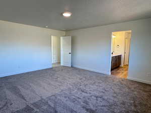 Unfurnished bedroom with dark carpet, a textured ceiling, and ensuite bathroom