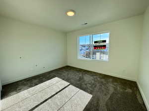 Unfurnished room featuring dark colored carpet and baseboards