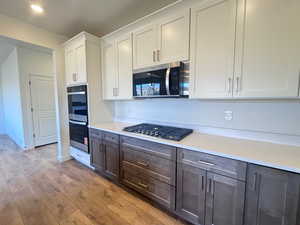Dual tone kitchen with dual tone cabinets, stainless steel appliances, light wood-type flooring, light stone countertops, and recessed lighting