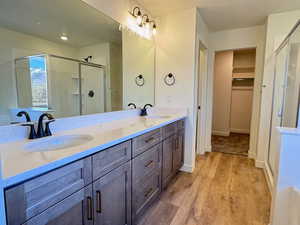 Full bath featuring a shower stall, double vanity, light wood-type flooring, a walk in closet, and a textured ceiling