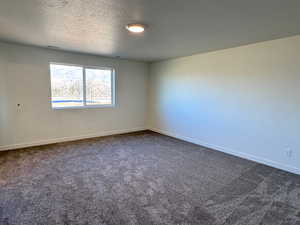 Unfurnished room featuring a textured ceiling and dark carpet