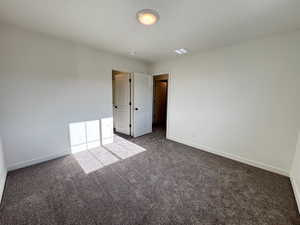 Unfurnished bedroom featuring dark colored carpet and baseboards