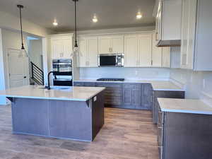 Two tone kitchen with two tone color scheme, stainless steel microwave, light stone counters, double oven, and dark wood-type flooring