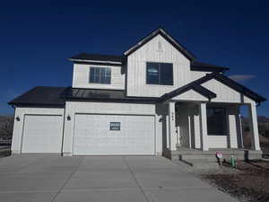 Modern farmhouse featuring a standing seam roof, driveway, covered porch, and an attached garage
