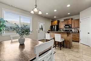 Kitchen featuring wood finish cabinets, a kitchen bar, a chandelier, an island with sink, and dark stone countertops