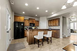 Kitchen featuring a kitchen breakfast bar, wood finish cabinets, black appliances, a center island, and a ceiling fan