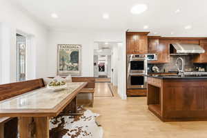Kitchen with double oven, light wood finished floors, dark stone counters, recessed lighting, and decorative backsplash