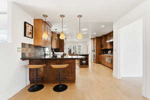 Kitchen featuring decorative light fixtures, a kitchen bar, wood finish cabinetry, light wood-style flooring, and dark stone countertops