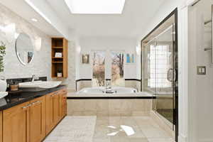 Full bath featuring vanity, a skylight, a stall shower, a garden tub, and light tile patterned floors