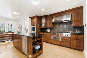 Kitchen with an island with sink, open shelves, light wood-type flooring, recessed lighting, and a warming drawer