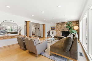Living room featuring ornamental molding, light wood finished floors, recessed lighting, decorative columns, and a stone fireplace