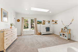 Bedroom with a skylight, a nursery area, light carpet, and recessed lighting