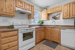 Kitchen with white appliances, dark countertops, and light wood finish cabinetry