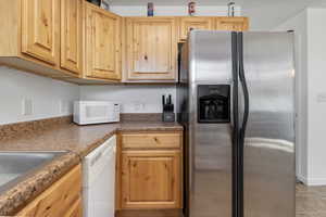 Kitchen featuring white appliances, light wood finish cabinetry, and dark countertops