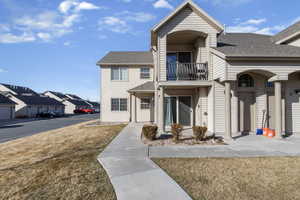 View of front of home with a balcony, roof with shingles, a front yard, and a residential view