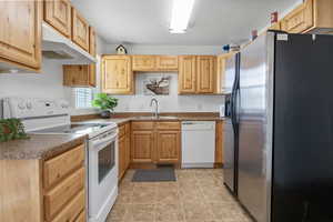 Kitchen with white appliances, light wood finish cabinets, dark countertops, and a textured ceiling