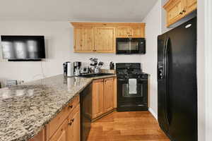 Kitchen featuring black appliances, light stone counters, light wood finished floors, and light wood finish cabinets