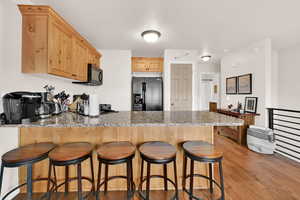 Kitchen with a breakfast bar, a peninsula, light wood finish cabinets, and black fridge