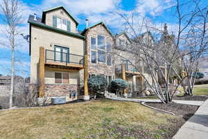 View of front facade with stone siding, a front lawn, and a balcony