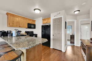 Kitchen featuring a breakfast bar, a peninsula, black appliances, light wood-style flooring, and a textured ceiling