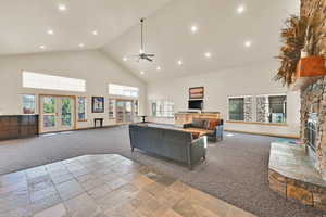 Living room featuring light carpet, stone tile flooring, a ceiling fan, recessed lighting, and a stone fireplace