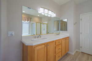 Full bathroom featuring double vanity, a stall shower, and light wood-style flooring