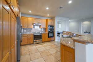 Kitchen featuring double ovens, recessed lighting, backsplash, light granite counters, and a kitchen bar