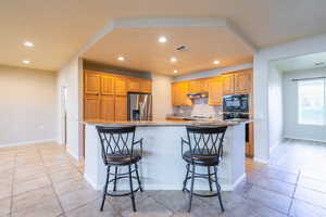 Kitchen featuring tile backsplash, a large island, light granite counters, a kitchen breakfast bar, and recessed lighting