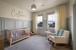 Carpeted bedroom featuring a decorative wall, a crib, and a wainscoted wall