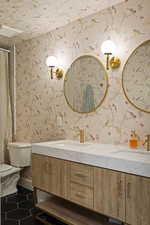 Bathroom with double vanity, dark tile patterned floors, and wallpapered walls