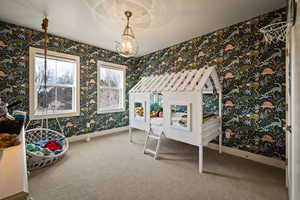 Bedroom with light colored carpet, wallpapered walls, and suspended lighting