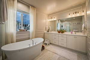 Full bath with double vanity, a freestanding bath, plenty of natural light, a decorative wall, and a stall shower