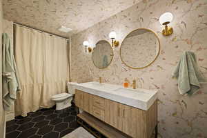 Bathroom featuring double vanity, wallpapered walls, a shower with curtain, and dark tile patterned floors